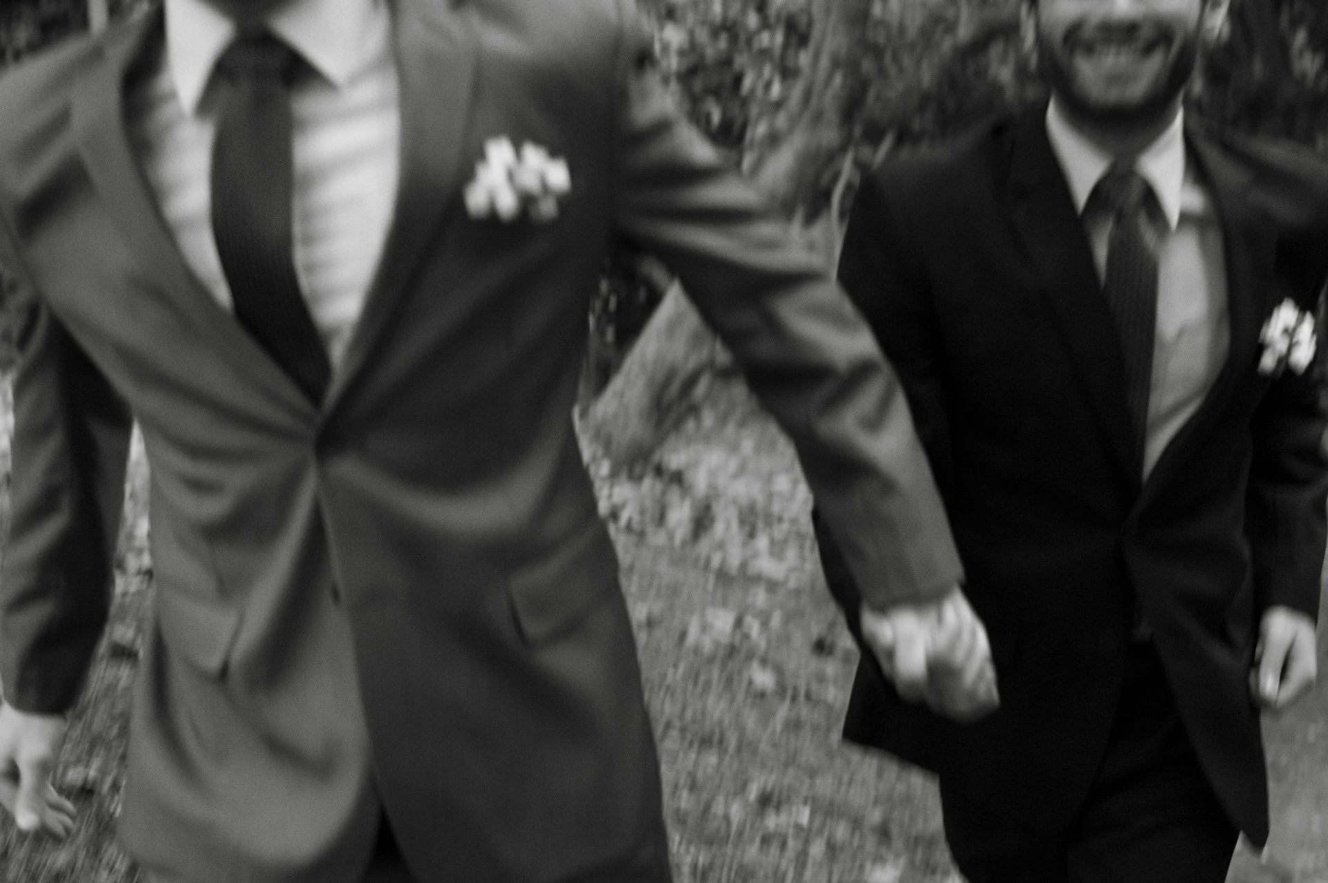 Two grooms in suits with boutonnieres holding hands as they walk together outdoors