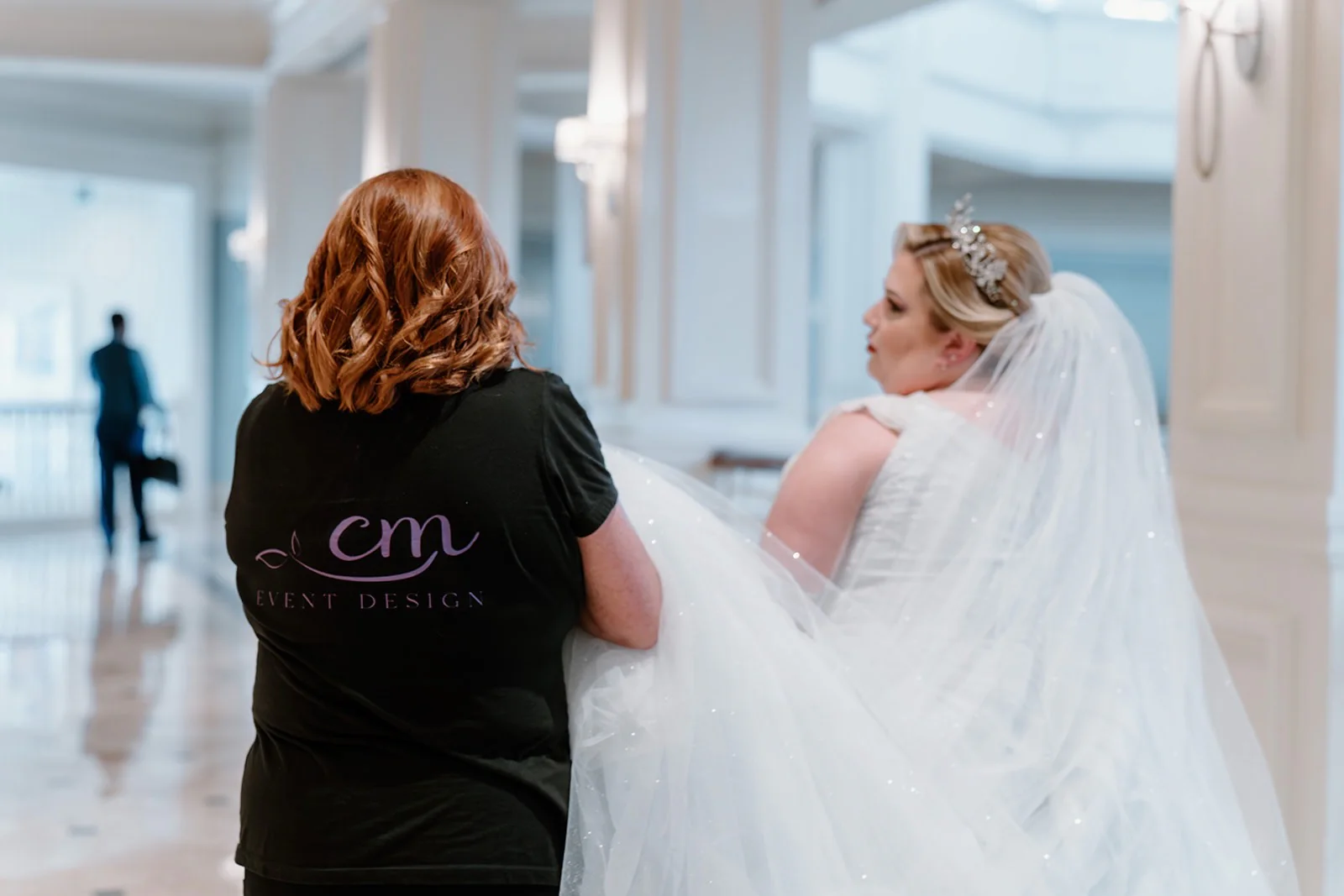 A CM Event Design planner carrying the bride's gown and veil as she walks to the ceremony.