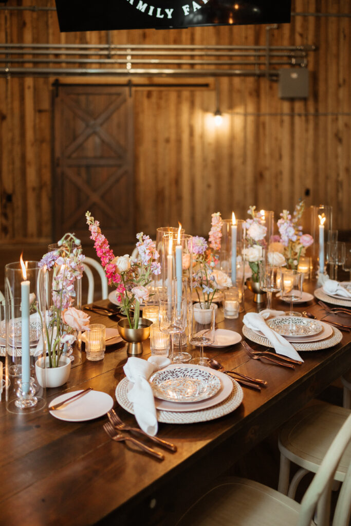 Candlelit wedding reception tablescape with pastel florals in a rustic barn venue