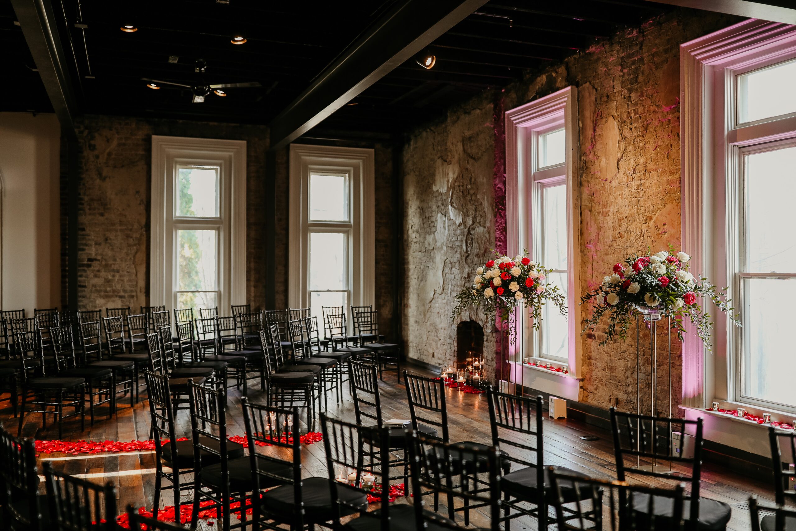 Wedding ceremony set with black chairs and floral arrangements in a brick venue