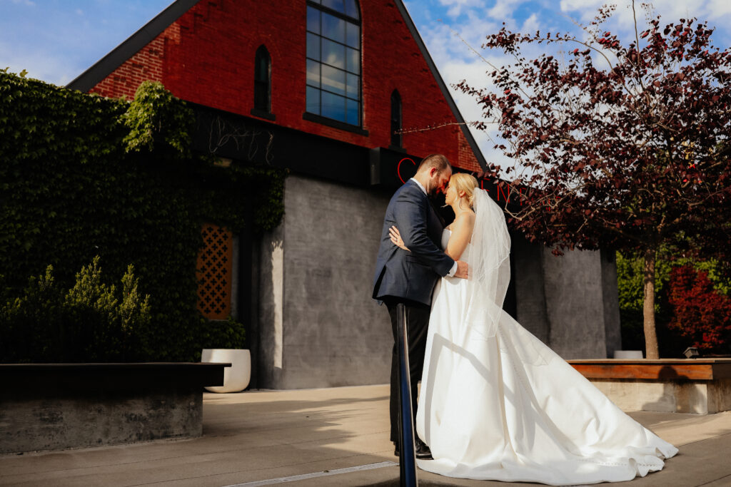 Bride and groom embracing outside a brick wedding venue on a sunny day