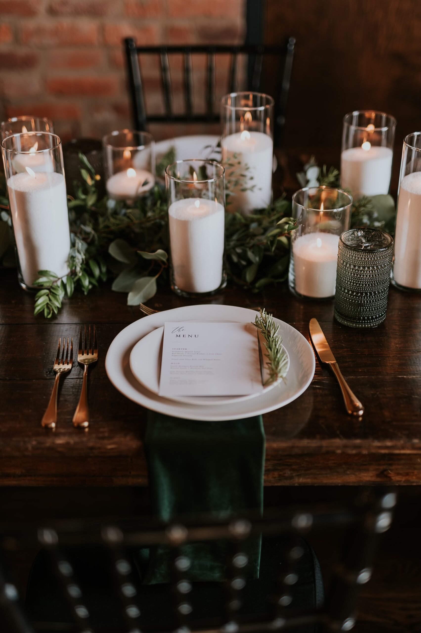 Wedding place setting with menu card candles and greenery on a wood table