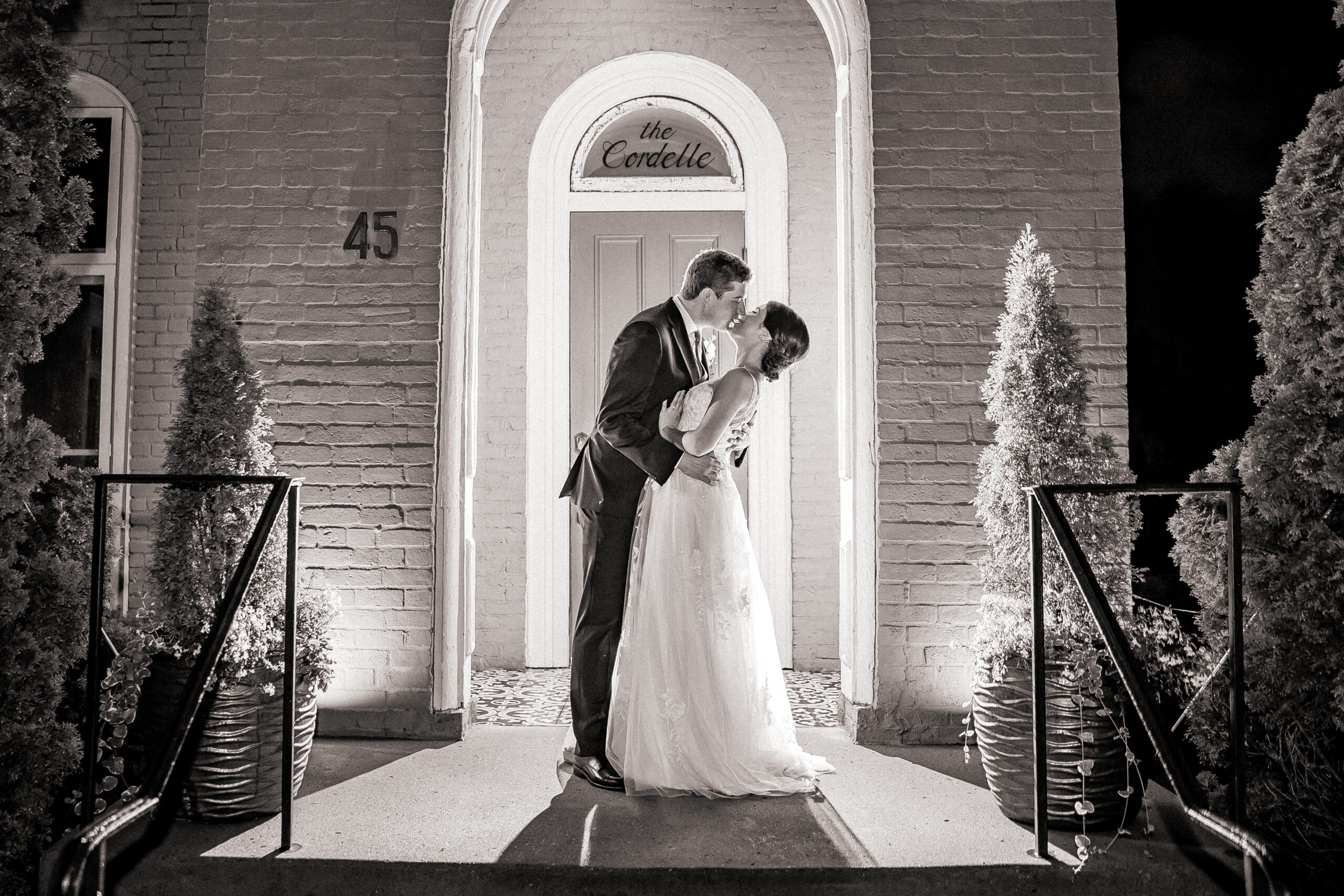 Black and white photo of newlyweds kissing at a brick wedding venue entrance